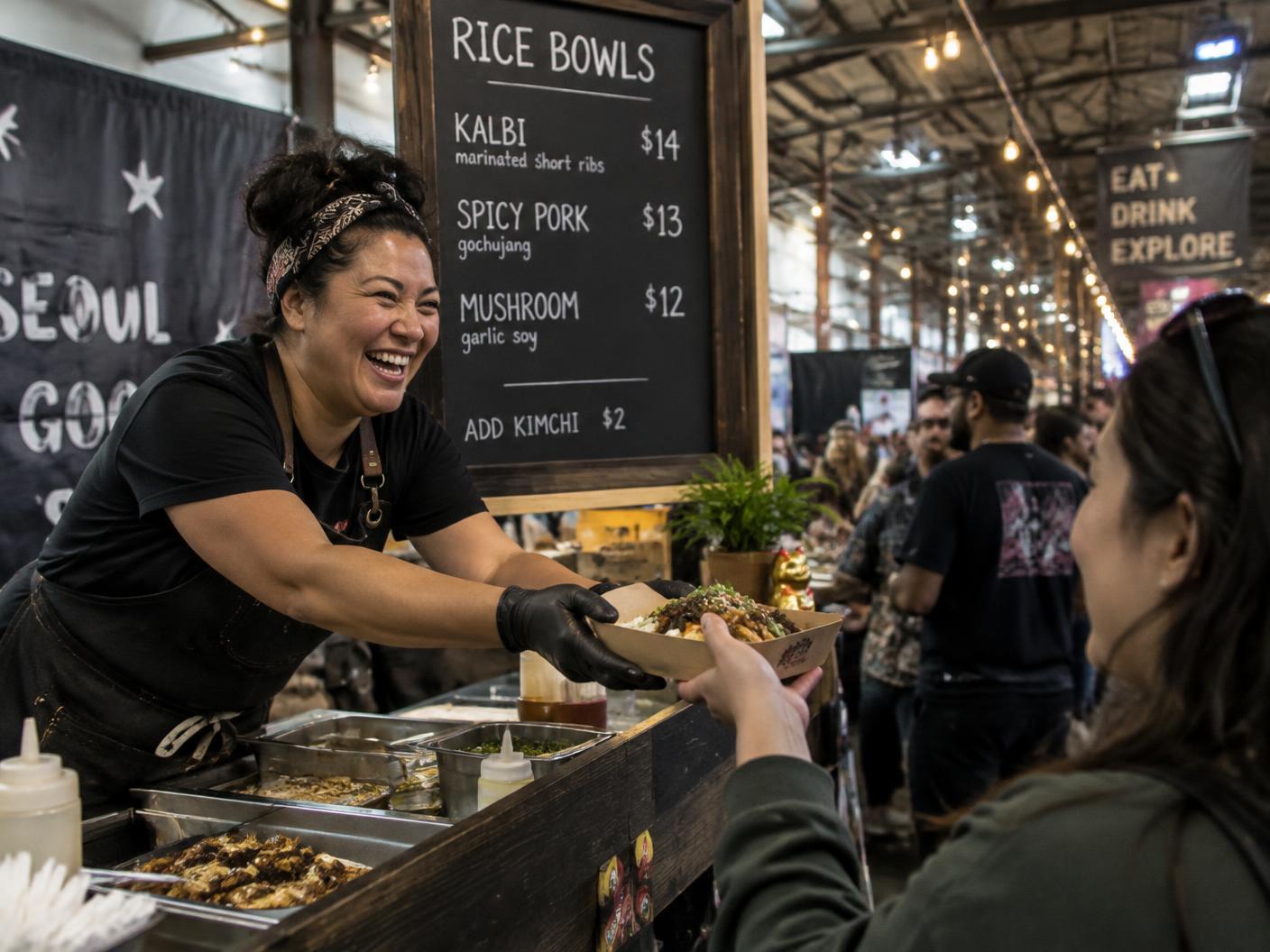 A laughing cook leaning over an indoor food hall counter to hand a tray of food to a visitor